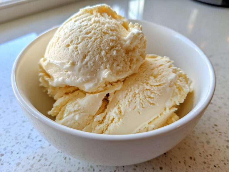 Two scoops of creamy, pale yellow protein ice cream served in a small white bowl.