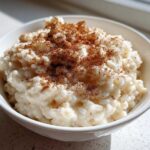 Close-up of creamy rice pudding topped generously with ground cinnamon in a white bowl.