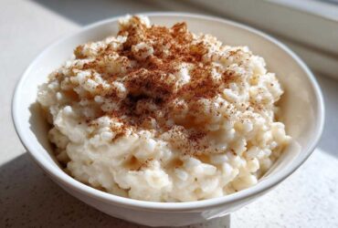 Close-up of creamy rice pudding topped generously with ground cinnamon in a white bowl.