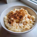 Close-up of creamy rice pudding topped generously with ground cinnamon in a white bowl.