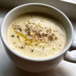 Close-up of creamy roasted cauliflower soup topped with cracked black pepper and olive oil drizzle.