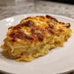 A thick, creamy slice of scalloped potatoes featuring layers of tender potato and a deeply browned, cheesy crust.