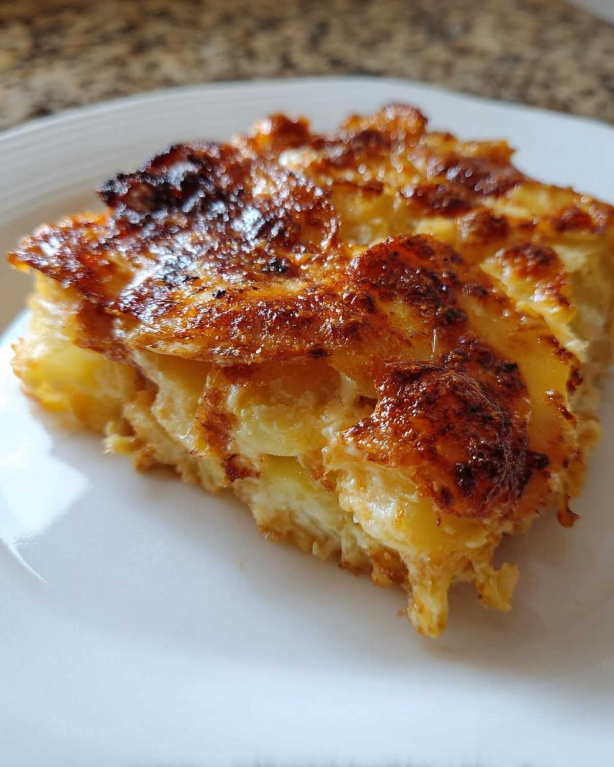 A close-up of a rich slice of creamy scalloped potatoes featuring layers of tender potatoes and a deeply browned, cheesy top.