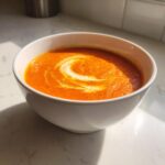 A close-up of a bowl of creamy tomato basil soup, garnished with a swirl of cream.