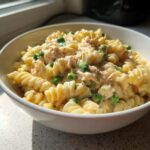 Close-up of creamy tuna pasta made with fusilli, mixed with green peas, served in a white bowl.