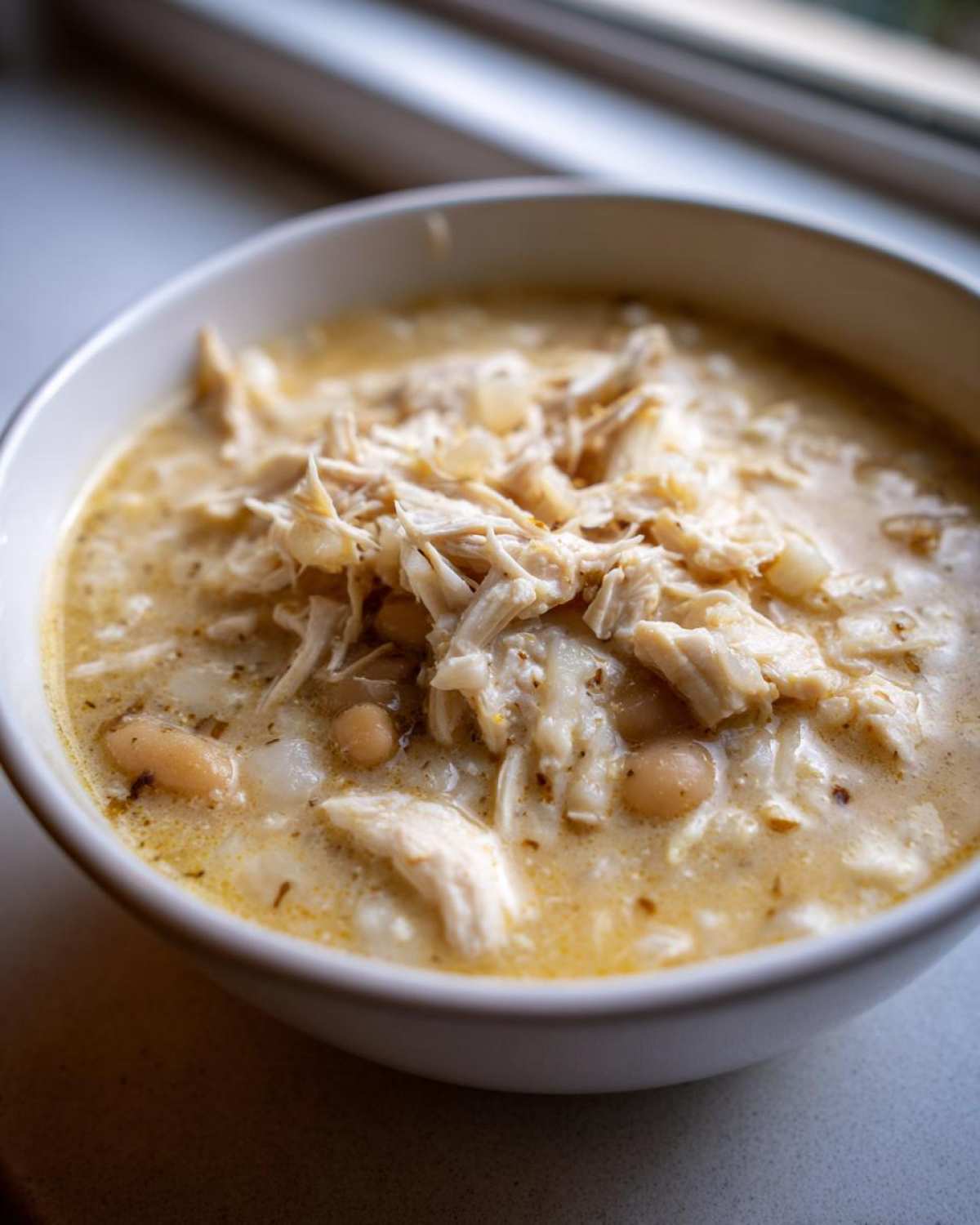 Close-up of a white bowl filled with creamy white chicken chili, featuring shredded white chicken and white beans.