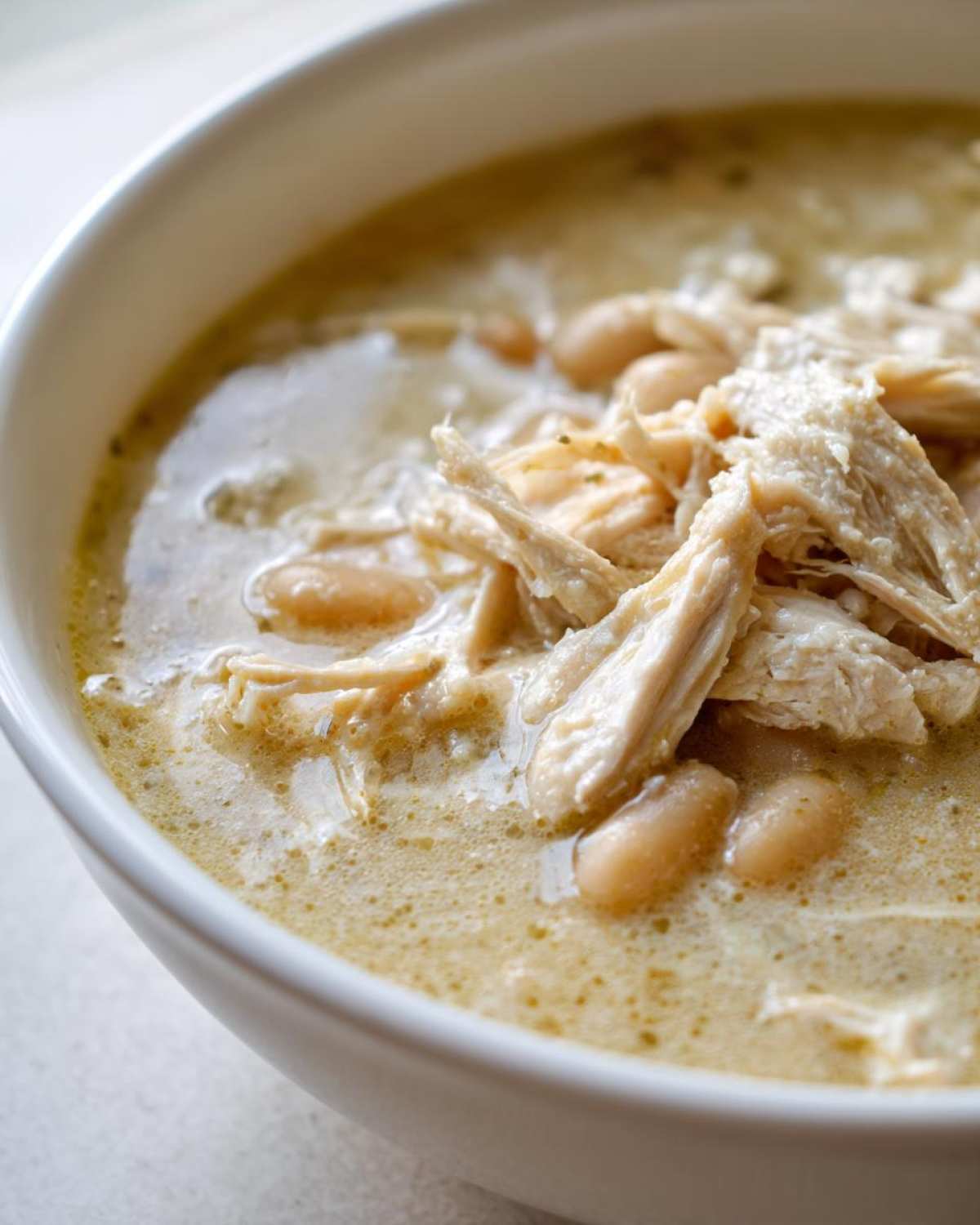 Close-up of a creamy white chili featuring shredded white chicken and cannellini beans.