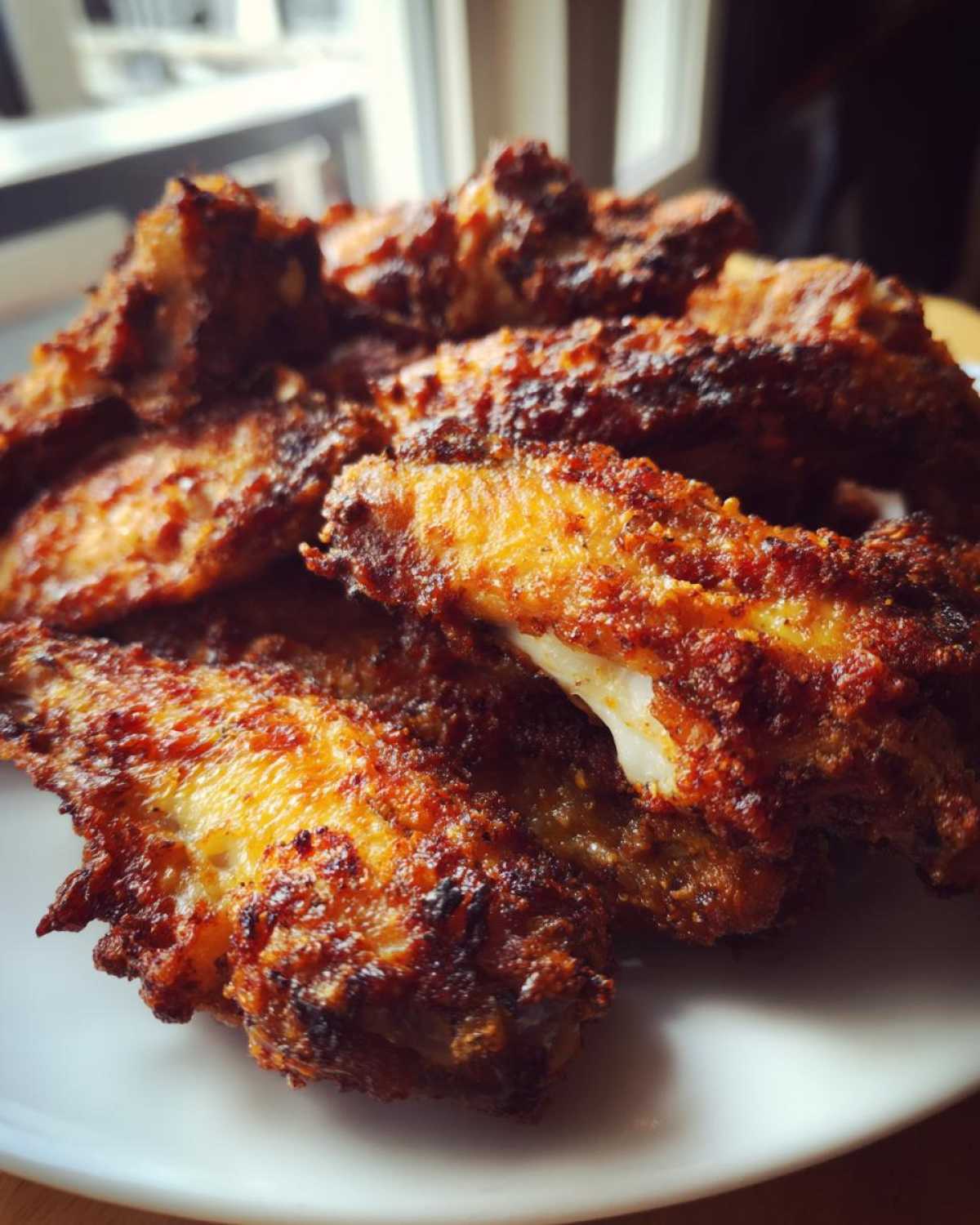 Close-up of a pile of intensely browned, crispy baked chicken wings on a white plate.