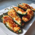 Close-up of several baked Jalapeño poppers, halved and stuffed with creamy cheese and topped with golden brown breadcrumbs.