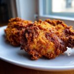Close-up of two pieces of golden brown, crispy fried chicken served on a white plate.