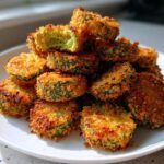 A close-up of a tall stack of golden brown, crunchy Fried Pickles on a white plate.