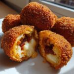 Close-up of crispy fried rice balls, one cut open revealing melted cheese and filling.