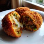 Close-up of a fried rice balls cut in half showing melted cheese and peas inside.