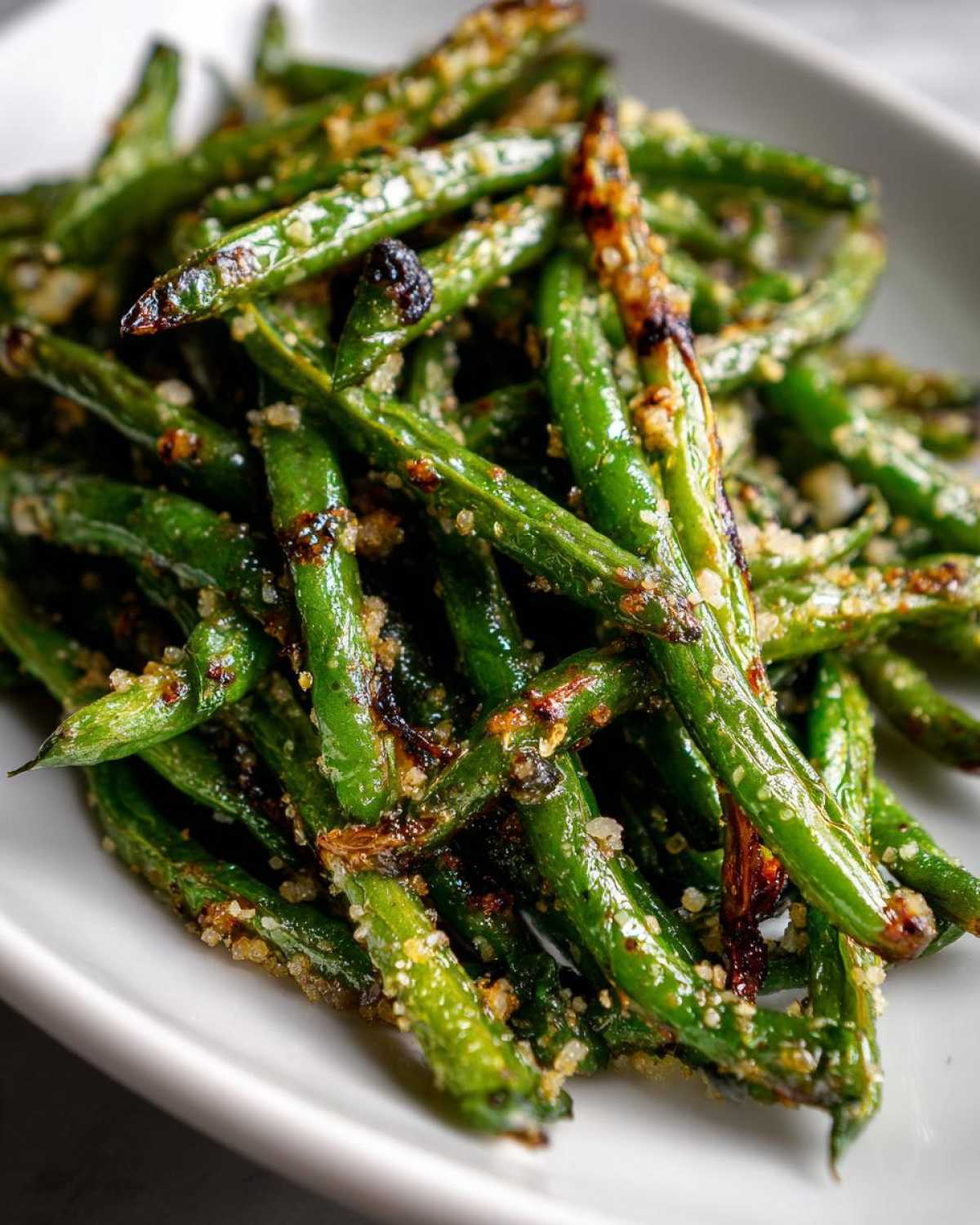 Close-up of perfectly roasted, bright green beans sprinkled with a savory, slightly browned topping.
