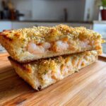 Two stacked pieces of crispy shrimp toast cut in half, showing the creamy shrimp filling and sesame seed topping.