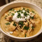 A close-up of a bowl of crockpot white chicken chili topped with sour cream and fresh cilantro.