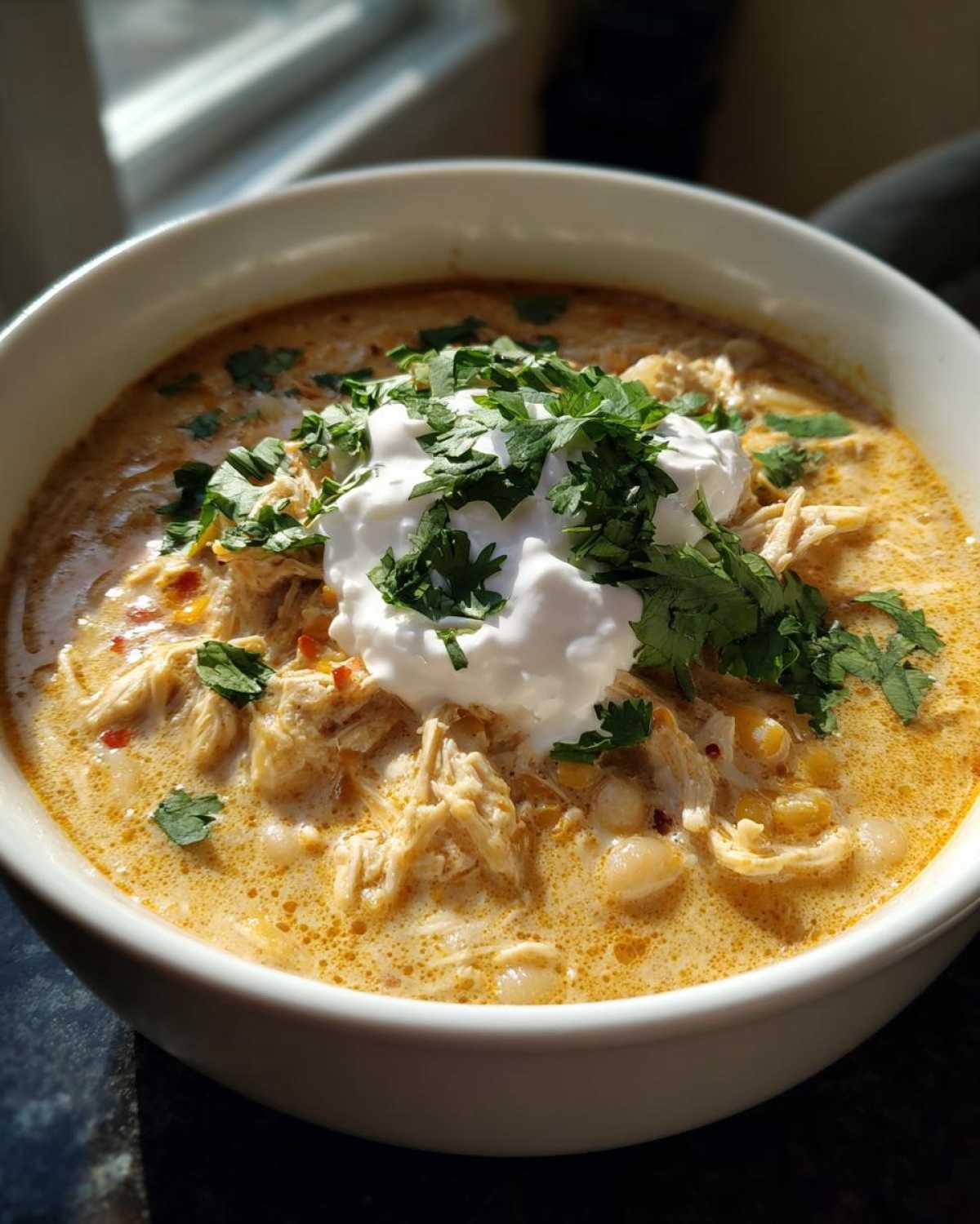 A close-up of a bowl of creamy crockpot white chicken chili topped with sour cream and fresh cilantro.