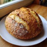 A golden-brown, round loaf of crusty Italian bread sitting on a white plate.