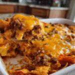 A spoonful of hot Dorito Casserole, loaded with ground beef and melted cheddar cheese, being lifted from the baking dish.