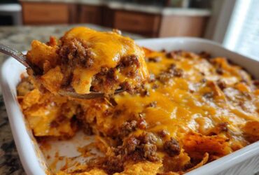 A spoonful of hot Dorito Casserole, loaded with ground beef and melted cheddar cheese, being lifted from the baking dish.