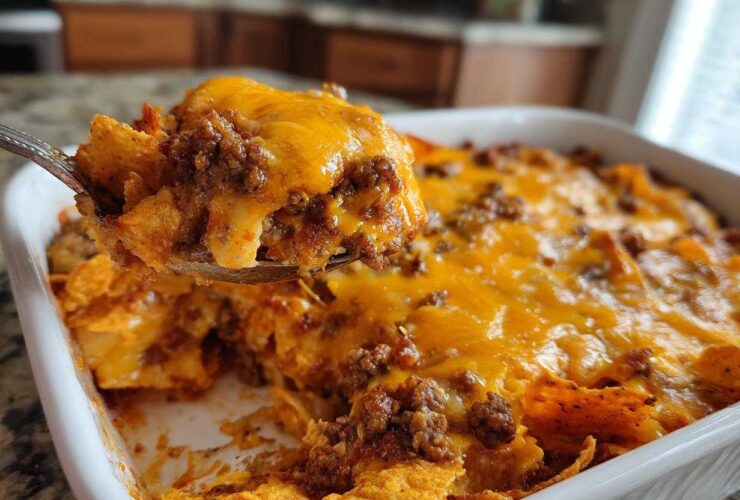 A spoonful of hot Dorito Casserole, loaded with ground beef and melted cheddar cheese, being lifted from the baking dish.
