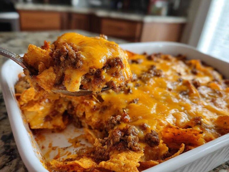 A spoonful of hot Dorito Casserole, loaded with ground beef and melted cheddar cheese, being lifted from the baking dish.