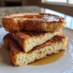 Three thick slices of easy french toast stacked, coated in cinnamon sugar and drizzled with maple syrup.