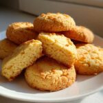 A stack of golden brown 3-ingredient butter cookies on a white plate, one cookie is broken open to show the crumb.