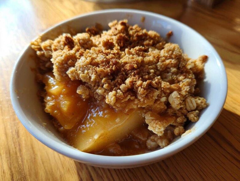 A close-up view of a warm serving of pear crisp in a white bowl, featuring bubbly fruit filling and a crunchy oat topping.