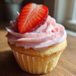 Close-up of a single, delicious strawberry cupcake topped with pink frosting and a fresh strawberry slice.
