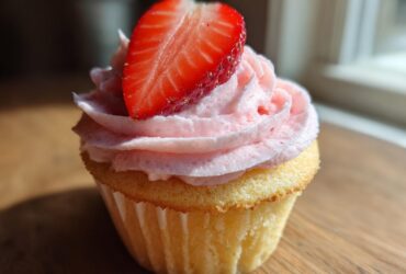 Close-up of a single, delicious strawberry cupcake topped with pink frosting and a fresh strawberry slice.