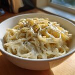 A white bowl filled with fettuccine pasta generously coated in creamy homemade alfredo sauce and sprinkled with herbs.