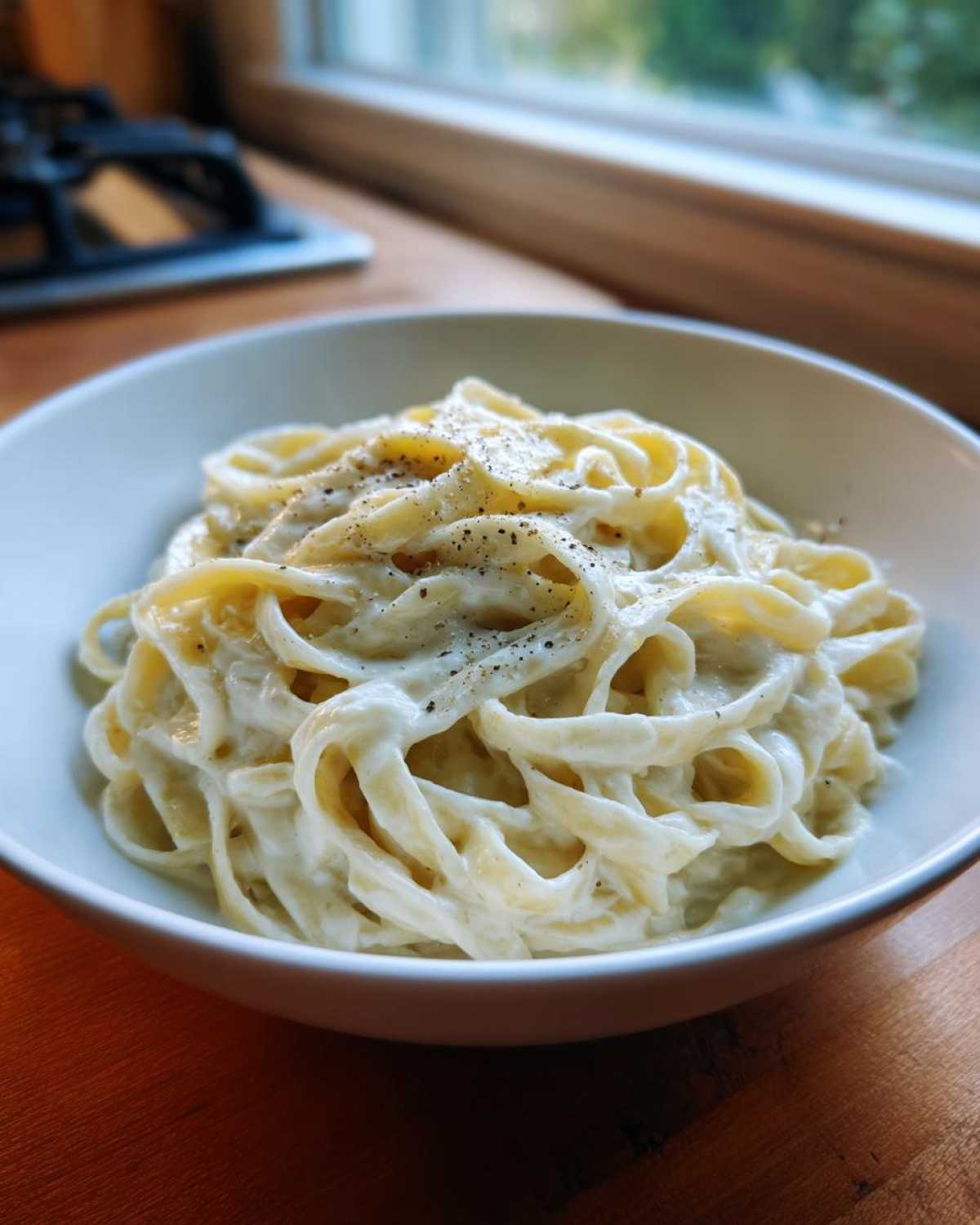A bowl of fettuccine pasta coated in rich homemade alfredo sauce and topped with black pepper.