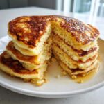 Close-up of a tall stack of fluffy almond flour pancakes, cut open to show the texture, drizzled with syrup.