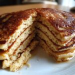 Close-up of a thick stack of golden brown almond flour pancakes cut open to show fluffy interior and drizzled with syrup.