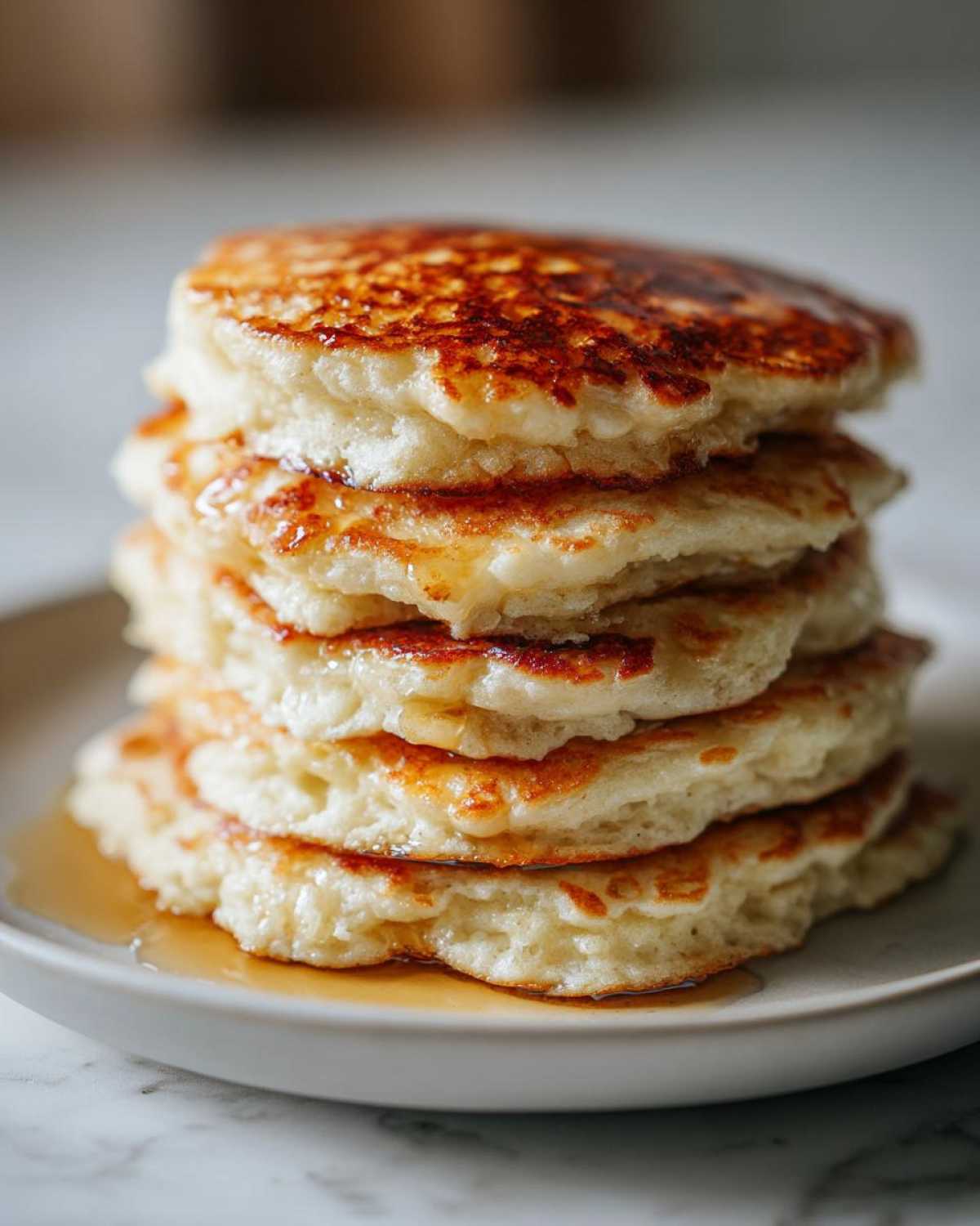A tall stack of five fluffy almond flour pancakes drizzled with golden syrup on a light plate.