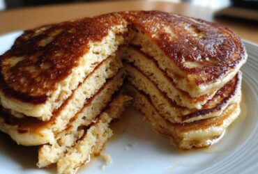 Close-up of a thick stack of golden brown almond flour pancakes cut open to show fluffy interior and drizzled with syrup.