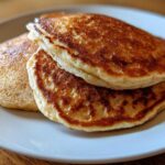 Close-up of two golden-brown almond flour pancakes stacked on a light plate.