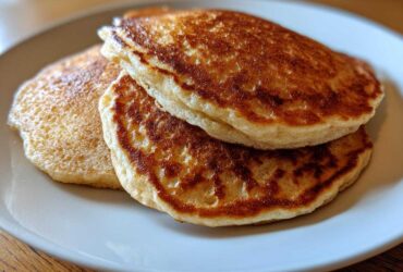 Close-up of two golden-brown almond flour pancakes stacked on a light plate.