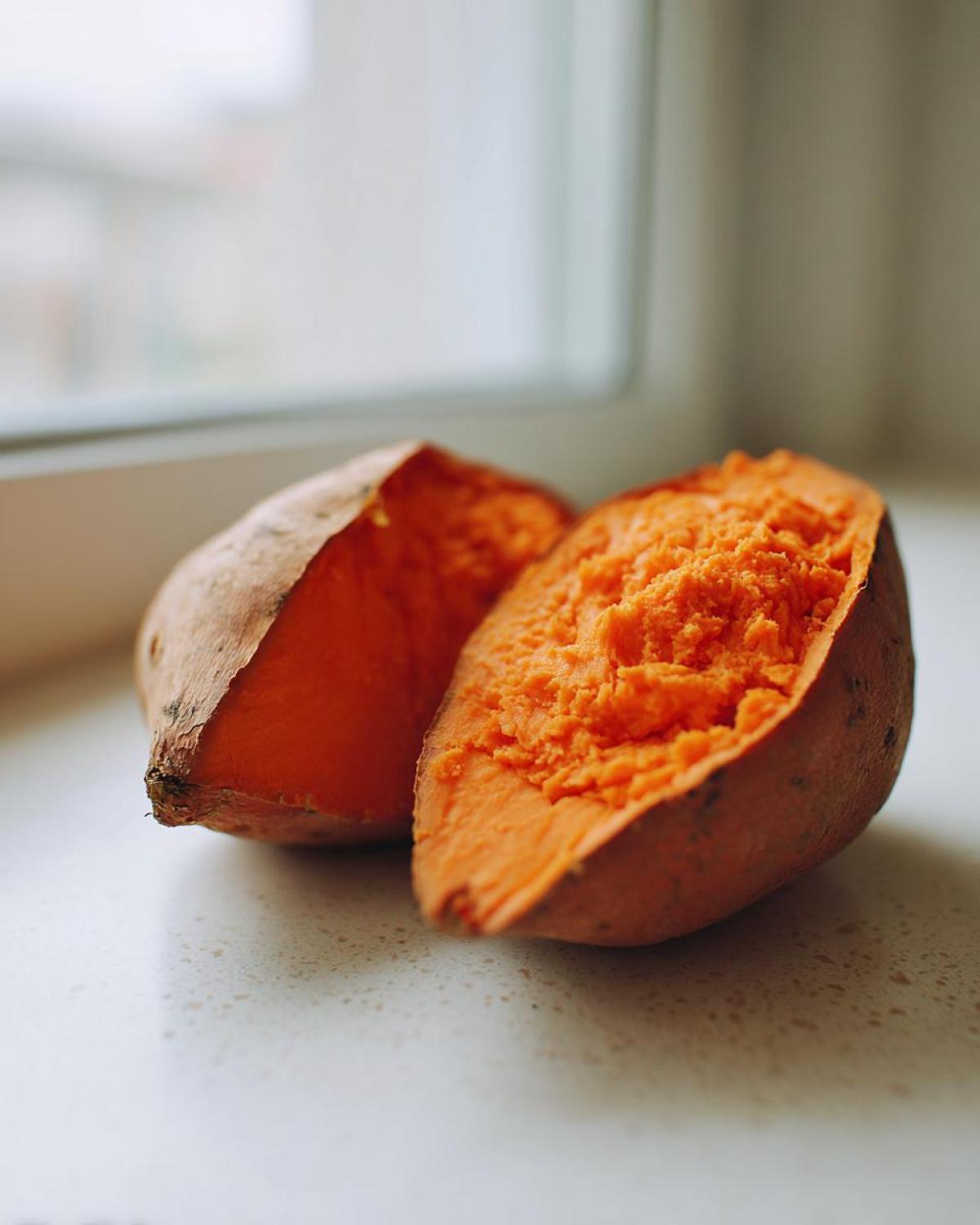 Close-up of a fluffy baked sweet potato cut in half, showing bright orange flesh.