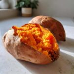 Close-up of a fluffy baked sweet potato split open, revealing bright orange, mashed interior.