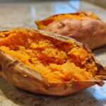 Close-up of a fluffy baked sweet potato split open, revealing bright orange, mashed interior flesh.