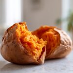 Close-up of a perfectly fluffy baked sweet potato split open, showing bright orange flesh.