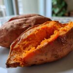 Close-up of a fluffy baked sweet potato split open, showing bright orange flesh sprinkled with sea salt.