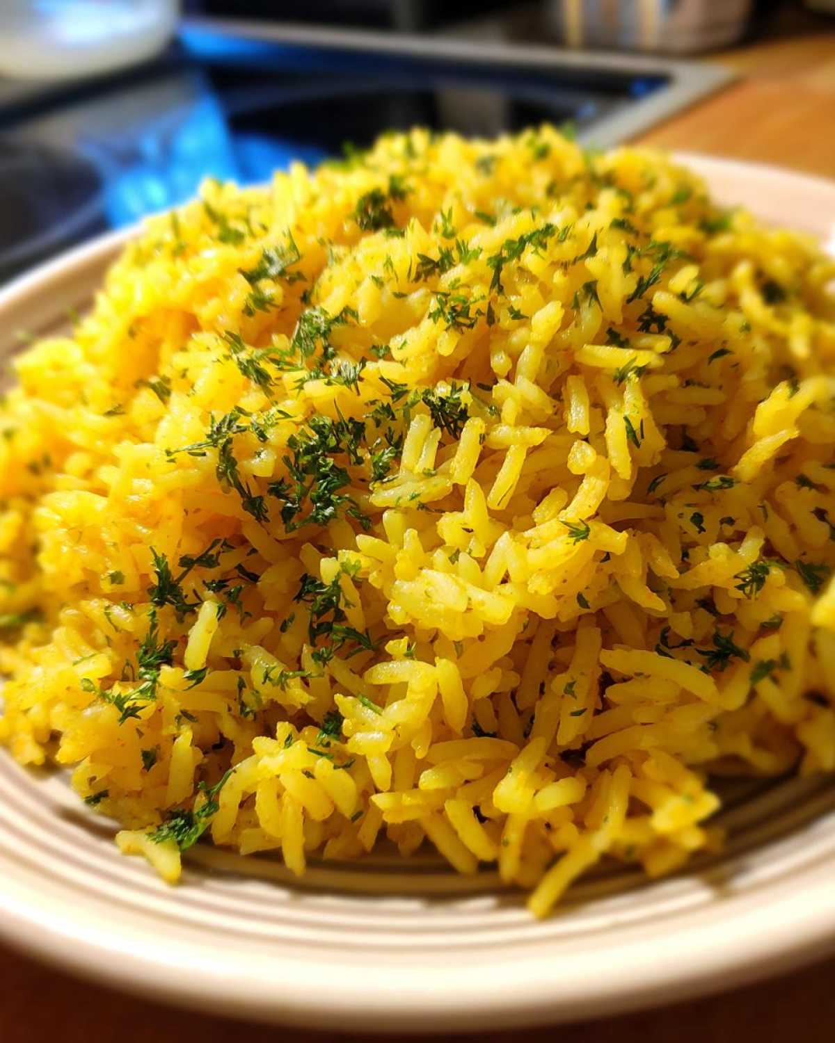 Close-up of fluffy, bright yellow mediterranean rice topped with chopped fresh parsley, served in a light-colored bowl.