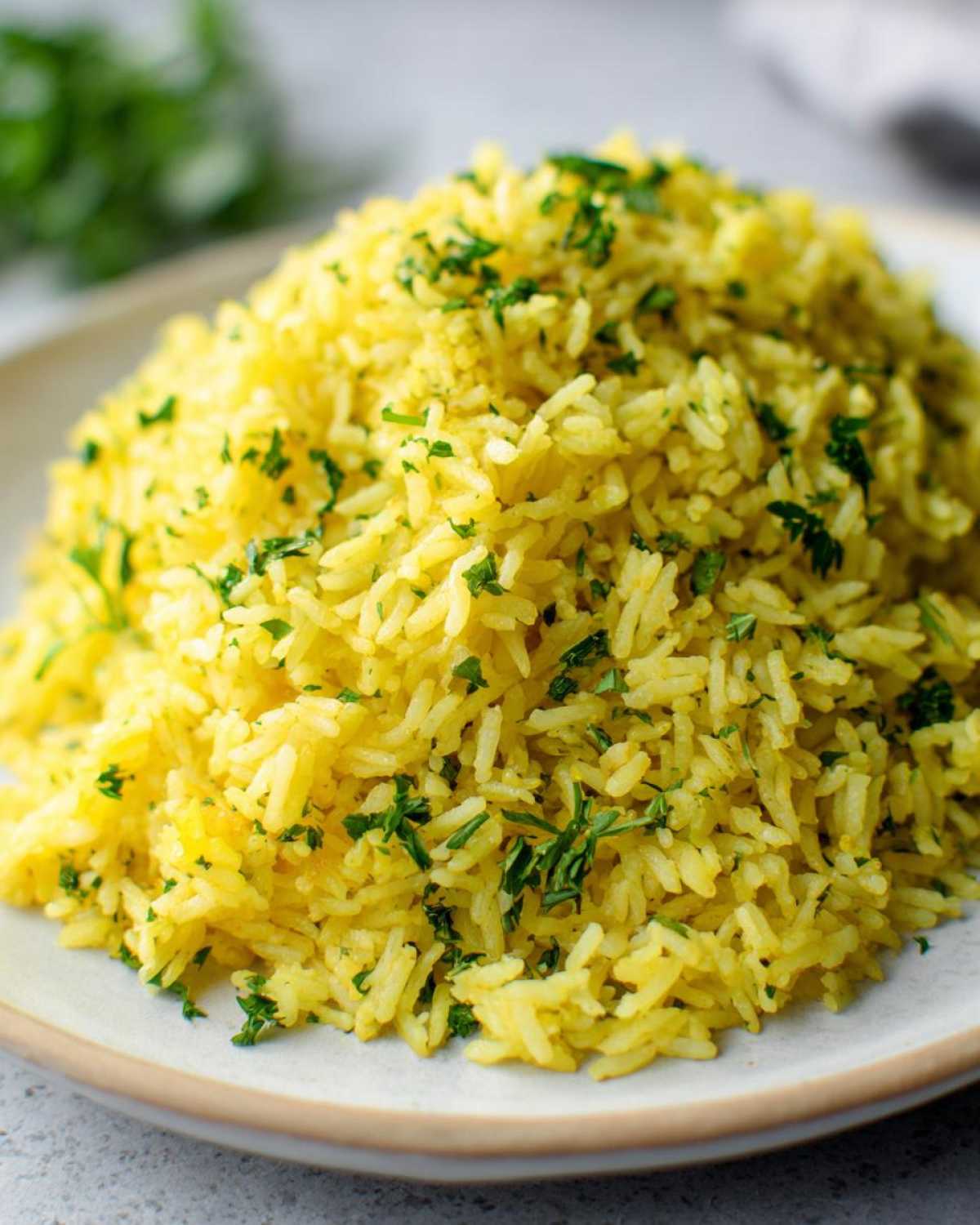Close-up of a mound of bright yellow mediterranean rice garnished with fresh chopped parsley on a light plate.