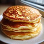A tall stack of four golden brown, very fluffy pancakes served on a white plate.