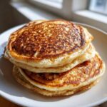 A close-up stack of three golden-brown, fluffy sourdough pancakes on a white plate.