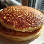 Close-up of a stack of fluffy sourdough pancakes with perfectly golden-brown, bubbly tops.