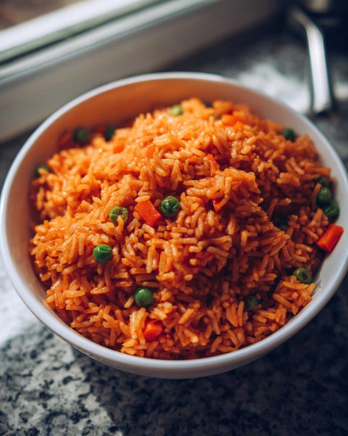 Close-up of a white bowl filled with fluffy, orange-tinted spanish rice mixed with green peas and diced carrots.